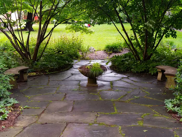 Flagstone patio with a stone planter and benches, surrounded by trees and shrubs