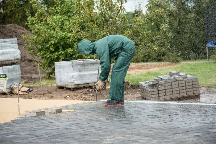 Worker in green coveralls laying concrete pavers on a prepared base