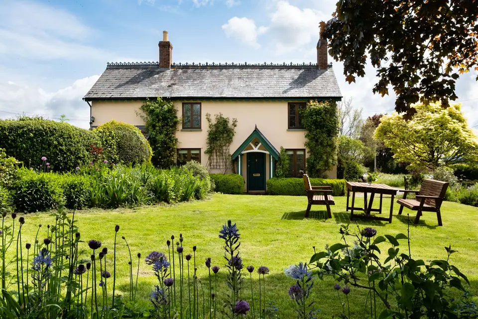 Mown lawn and flowering borders in front of a stone cottage