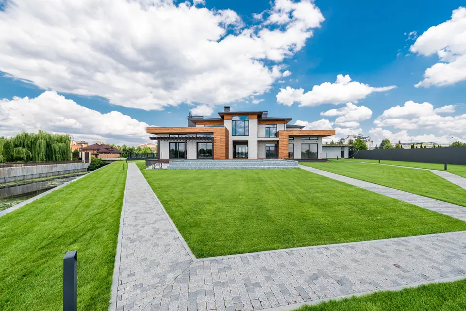 Wide mown lawn with stone paths leading to a modern house under a blue sky